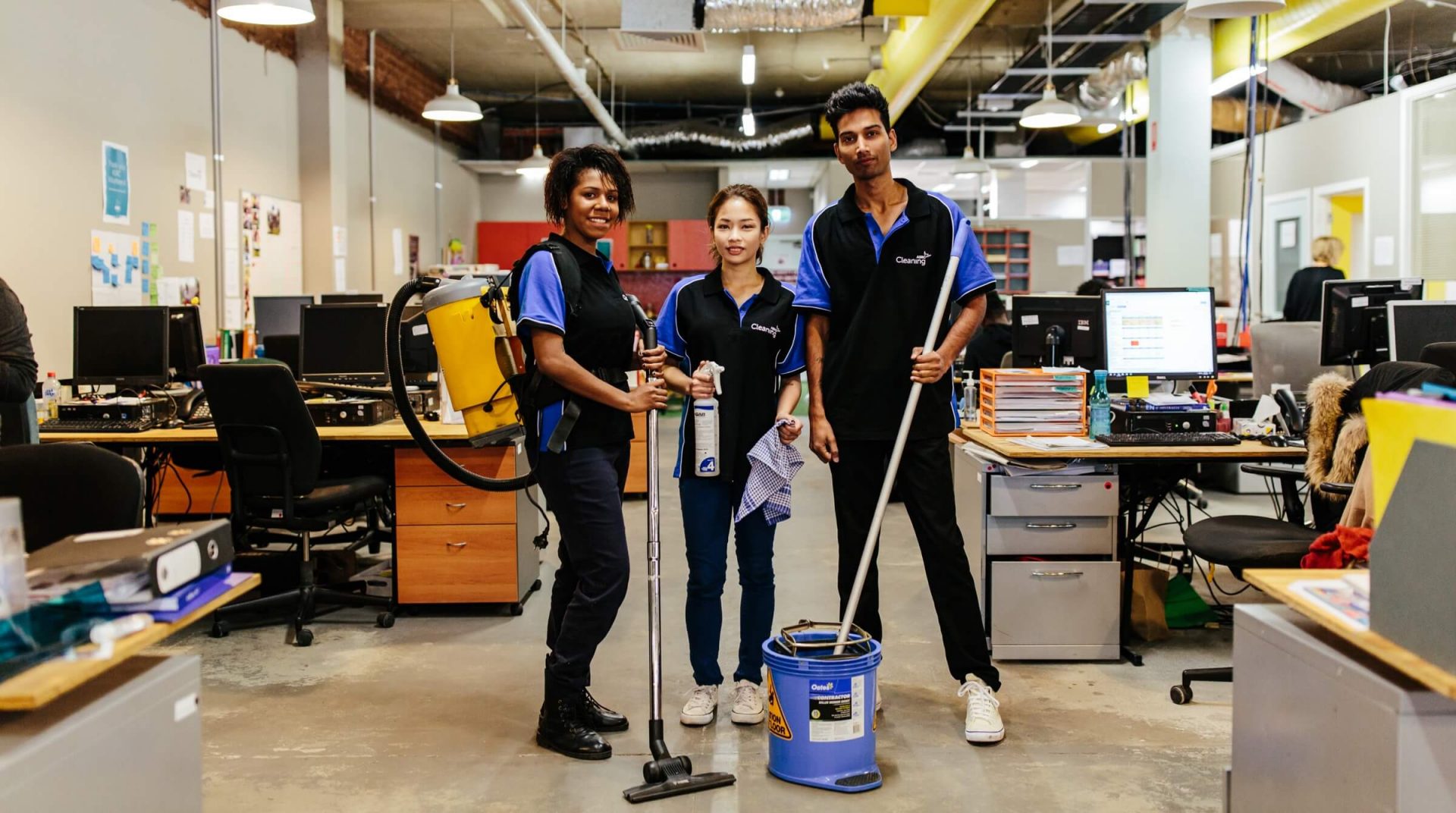 Image of three ASRC Cleaning staff members holding cleaning equipment in an office space
